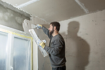 a male plasterer with a beard plasters a concrete wall with a spatula..