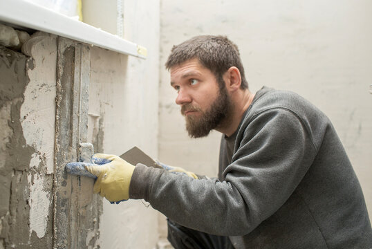 a male plasterer with a beard  in defocus  plasters a concrete wall with a spatula..