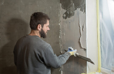 a male plasterer installs a perforated paint corner on the corner of the window slope and plasters...