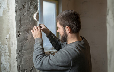 a man with a plasterer beard mounts a perforated painting corner on the corner of the doorway of...