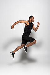 Fototapeta na wymiar full length of african american sportsman levitating while running on grey.