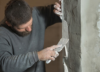 a man with a beard plasterer using a paint perforated corner plasters the corner of the doorway of...