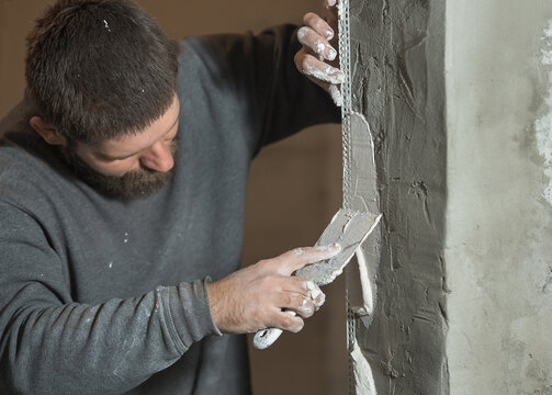 a man with a beard plasterer using a paint perforated corner plasters the corner of the doorway of the room
