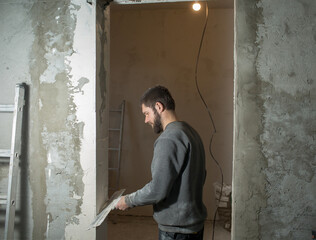 a man with a beard plasterer plasters a concrete corner of a doorway with a perforated corner with...
