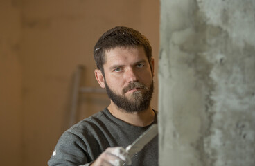 a man with a beard plasterer plasters with a spatula a concrete corner of a doorway with a...