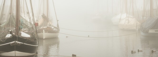 Elegant and modern yachts, sailing and fishing boats, small ships moored ti a pier in a thick fog....