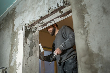 a man with a beard plasterer plasters a concrete corner of a doorway with a perforated corner with...