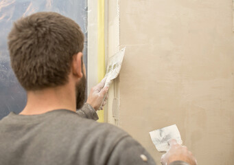 a man with a beard plasters window slopes with a spatula and putty..