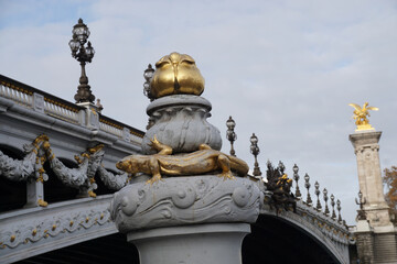 Fototapeta na wymiar closeup on gold salamander on pillar and bridge alexandre 3 with numerous lamp posts in paris france