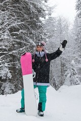Girl with a snowboard in the forest in the mountains and the snowfall
