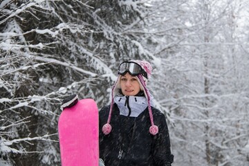 Girl with a snowboard in the forest in the mountains and the snowfall
