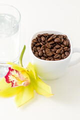 Obraz na płótnie Canvas Cup of coffee beans and glass of water with yellow orchid flower against a white background