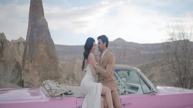 Beautiful photo shoot of the newlyweds in nature. Action. Nice views of the mountains and two loving people posing next to a pink car in nature in the summer.