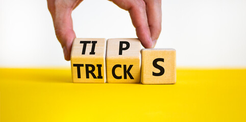 Tips and tricks symbol. Businessman turns wooden cubes and changes the word tricks to tips. Beautiful yellow table, white background. Business, tips and tricks concept. Copy space.