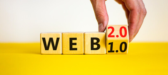 WEB 1.0 or 2.0 symbol. Businessman turns a wooden cube and changes words WEB 1.0 to WEB 2.0. Beautiful yellow table, white background, copy space. Business, technology and WEB 1.0 or 2.0 concept.