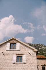 Stone house with white shutters on the windows at the foot of the mountain against the background of the sky