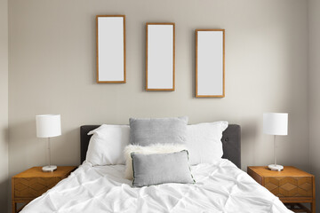 Detail shot of a cozy bedroom with white bedding and grey pillows, pictures of leaves above the bed, and lamps on wooden nightstands. Picture frames are blank.