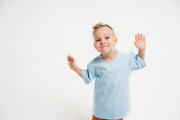 A boy in a blue T-shirt on a monochromatic background. The kid wriggles and dances. A place for text about children. Cheerful child with blonde hair