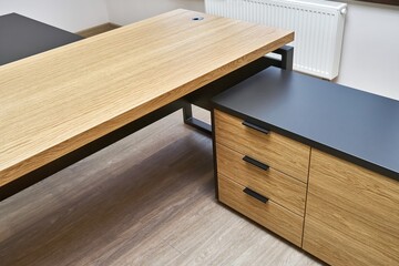 Large executive desk made of oak timber veneer with dark grey enamel in trendy minimal style stands in light spacious office closeup view