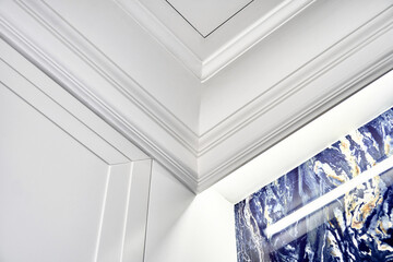 Part of elegant ceiling with LED backlight behind crown molding and small inspection hatch over blue marble wall in bathroom closeup low angle shot