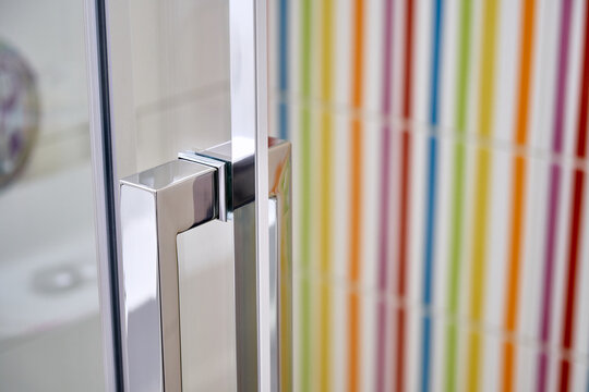 Closed glass door with stylish metal handle of contemporary shower cabin in bathroom with colorful tiles on wall close view