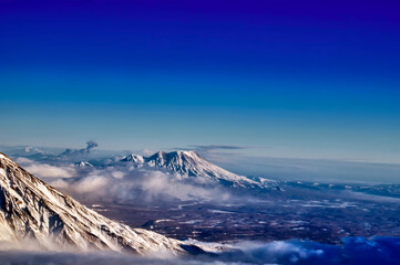 Mountain landscape with an erupting volcano. View from the airplane window