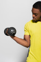 strong african american sportsman working out with dumbbell isolated on grey.