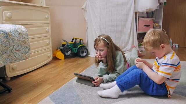 Boy and girl with phone and tablet at home on the floor