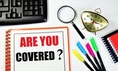 Are you covered? An inscription in the planning folder, against the background of a time control clock, magnifying glasses for research, a computer keyboard, colored markers and a notepad.