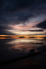 Dramatic clouds and sunrise over the water this tranquil winter morning by the lake. Silhouette of...