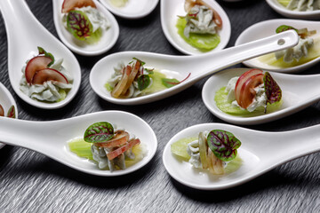 A light meat snack decorated with grapes, celery and leaves, in a dessert spoon is on the table.