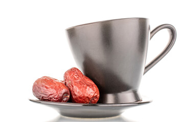 Two sweet dried ziziphus berries on a saucer with a black cup, close-up, isolated on white.