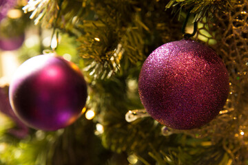 Detail of a red decorative ball hanging from an artificial Christmas tree.