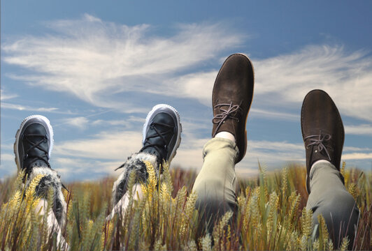 Pés de duas pessoas, uma adulta e uma criança deitadas no campo dentro das ervas - pés de fora, perna levantadas para cima - céu de fundo - divertimento  