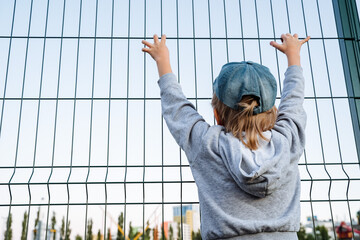 A little boy grabbed a fence on the playground. The boy watches the rides. Amusement park for children