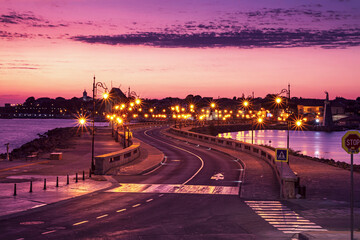 Obraz premium Evening city landscape - view of the road with street lights and the wooden windmill before the entrance to the Old Town of Nessebar, on the Black Sea coast of Bulgaria