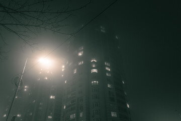 High rise residential buildings in the fog at night. Tall houses in dense fog