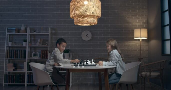 Little children playing chess and shaking hands at home in evening