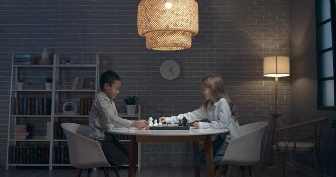 Little children playing chess at home in evening