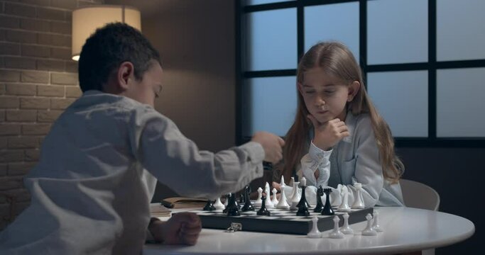 Little children playing chess at home in evening