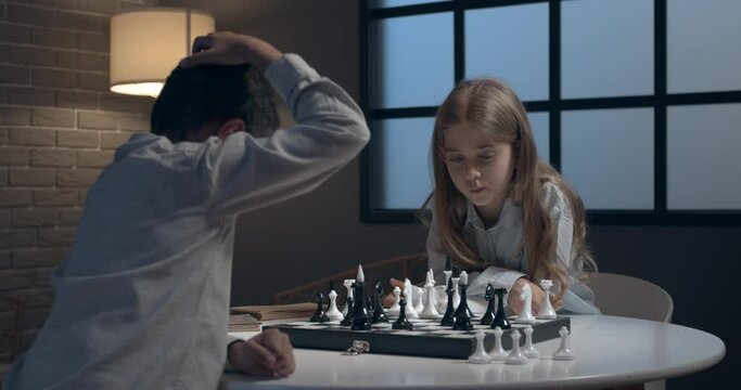 Little children playing chess at home in evening