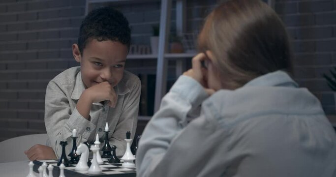 Little children playing chess at home in evening