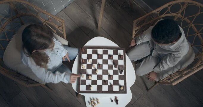 Little children playing chess at home in evening, top view
