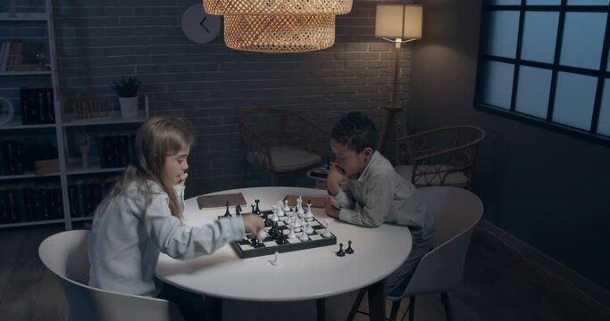 Little children playing chess at home in evening