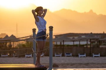 Happy woman relaxing outdoors on hotel deck on sea shore enjoying warm tropic evening. Summer vacations and travelling concept