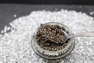 An open glass jar of sturgeon caviar. A teaspoon with caviar.