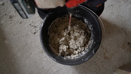 The worker mixes the self-leveling floor mortar in a bucket. Mix the solution in a bucket using a...