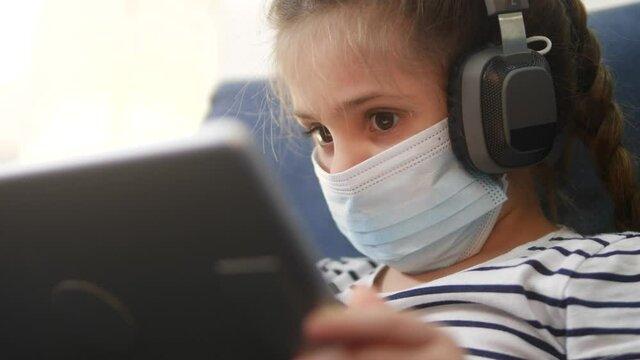 distance learning online a lessons. child girl with digital tablet in mask studying remotely at home. education coronavirus online lessons lockdown concept. school child learns distance learning