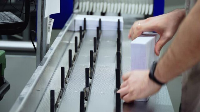 book production factory. printing of books at a specialized factory. the white man's hands gather the perfect stack of stitching sheets into a book. Conveyor production