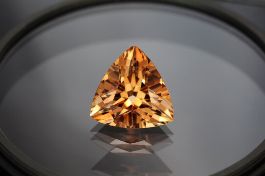 Imperial cognac color natural topaz gemstone setting for jewelry making. Light brown tea colour triangle faceted loose transparent gem. Heat treatment applied. Gemology mineralogy theme. Reflections.